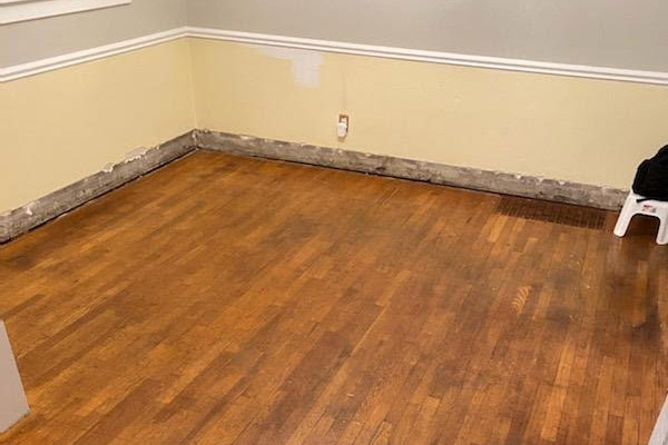 Empty room with damaged wooden flooring and skirting boards.